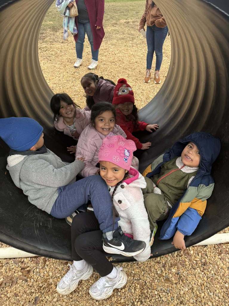 Students sit in a large pipe on a Christmas tree farm and smile.