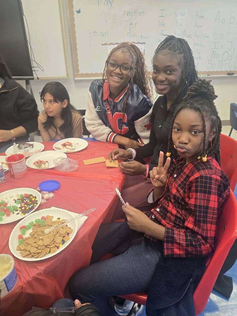 Minor Community School and Minor High School students pose for a photo while sitting at a table and making a gingerbread house.