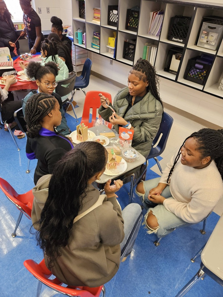 Students from Minor High School and Minor Community School sit at tables and make gingerbread houses.