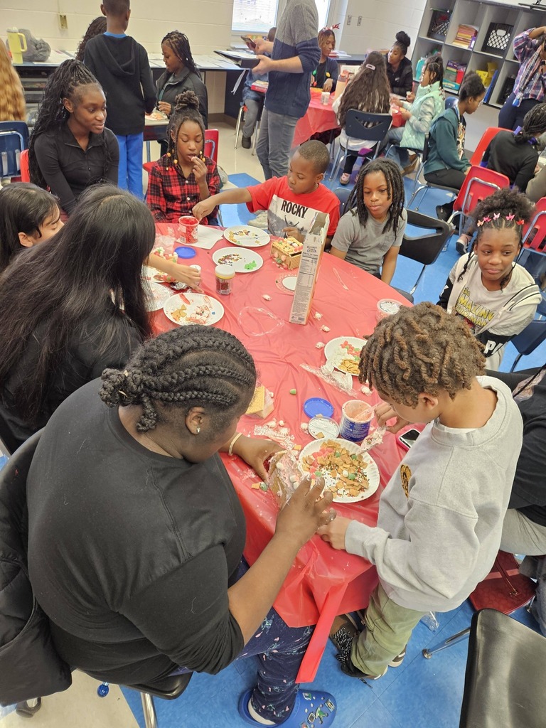 Students at Minor Community School and Minor High School sit together at a table in a classroom and make gingerbread houses.