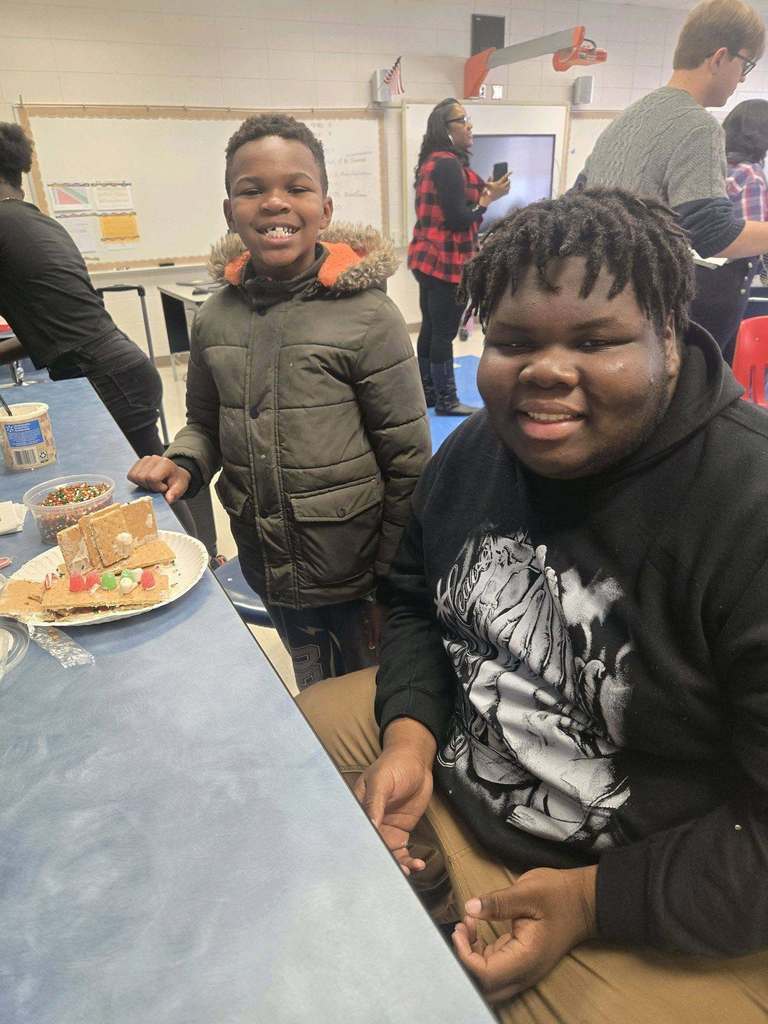 A Minor High School and Minor Community School student smile for a photo while making a gingerbread house.