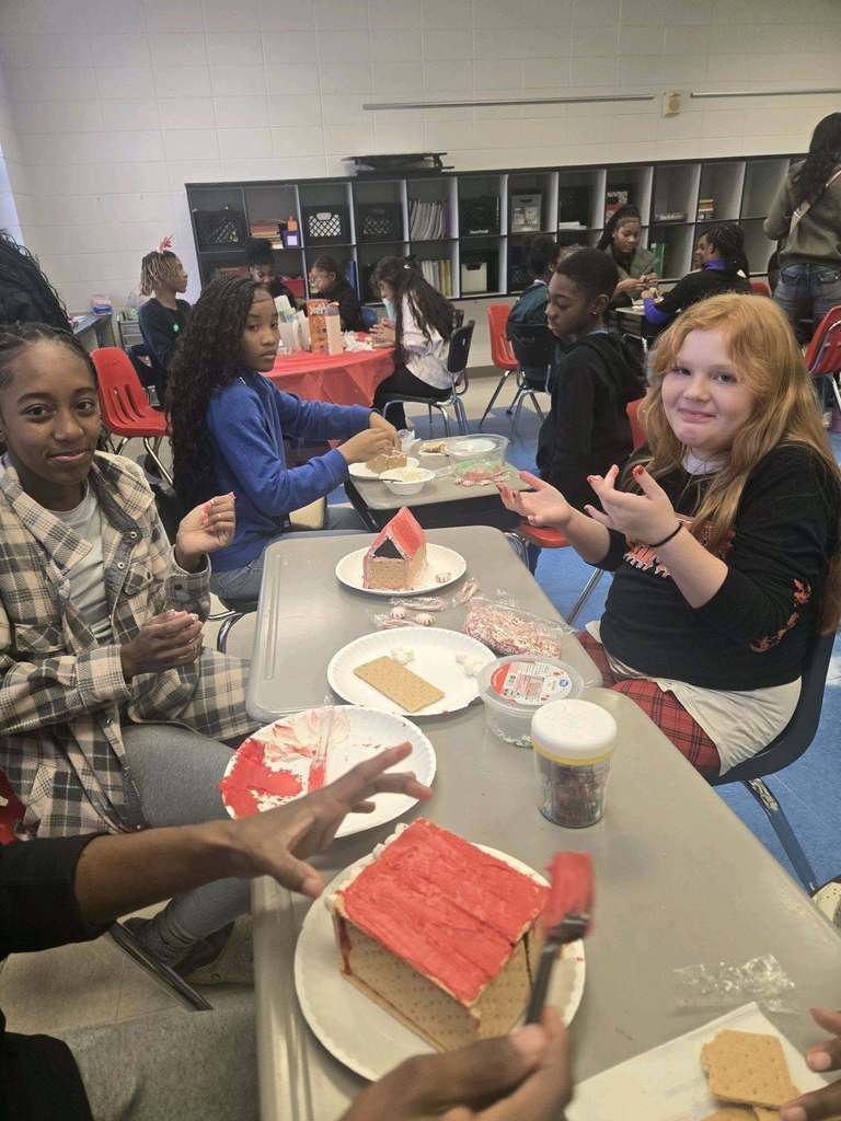 Students at Minor Community School and Minor High School sit together at a table in a classroom and make gingerbread houses.
