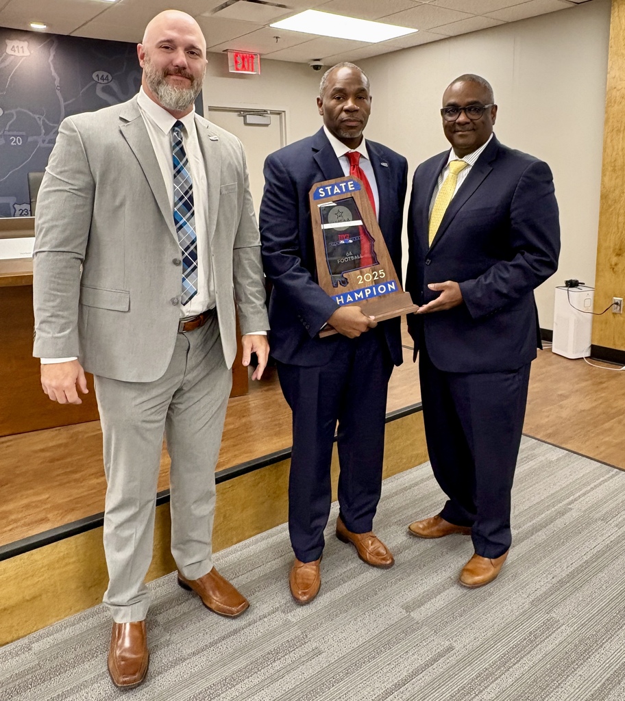 Clay-Chalkville High School Football Coach, Stuart Floyd,  CCHS Principal Dr. Eugene Dallas, and JEFCOED Superintendent Dr. Walter Gonsoulin stand together for a photo inside the Jefferson County Schools board room. Dr. Dallas holds Clay-Chalkville Football's 2025 State Championship trophy.