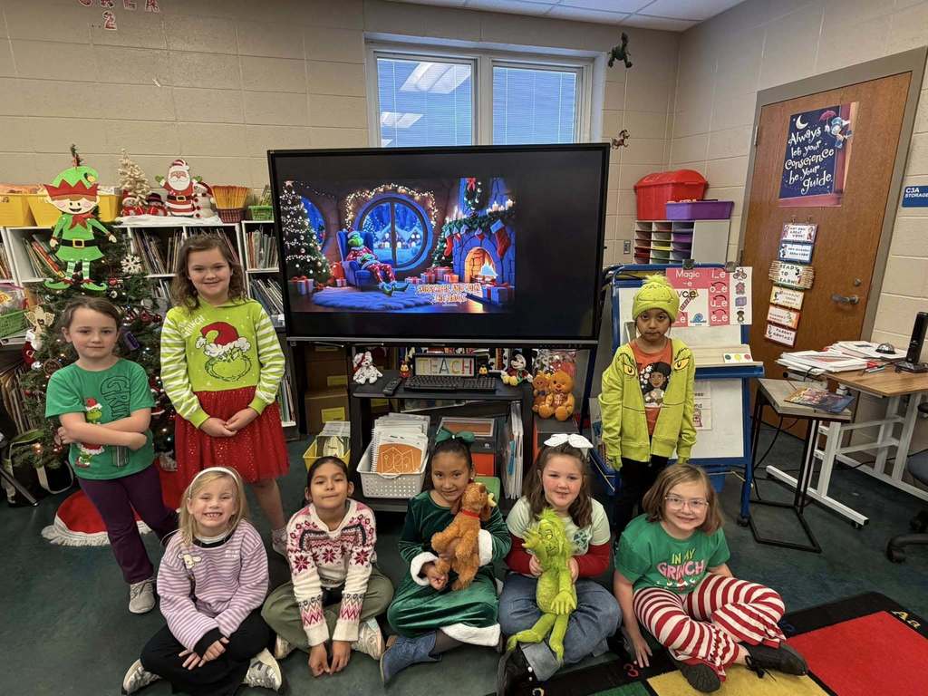 Students wearing Grinch-themed outfits pose for a photo inside a school library.