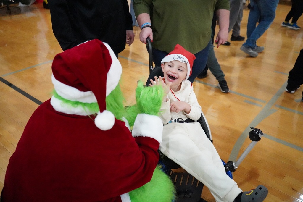 A student gives a person in a Grinch costume a high five while inside a school gym.