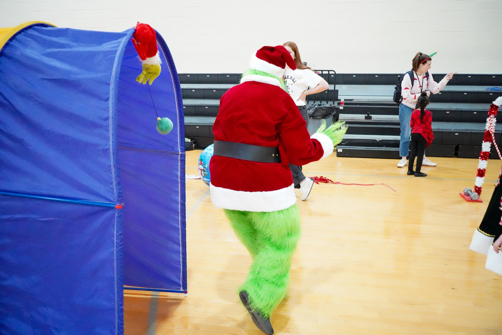 A person in a Grinch costume runs through an obstacle course set up inside a school gym.