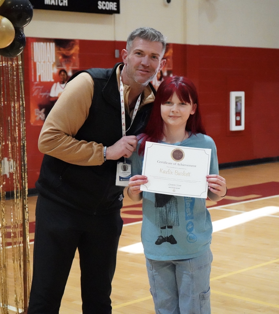 Rudd Middle School's principal poses for a photo with a student during an award ceremony in the school gym. The student holds a certificate and smiles.