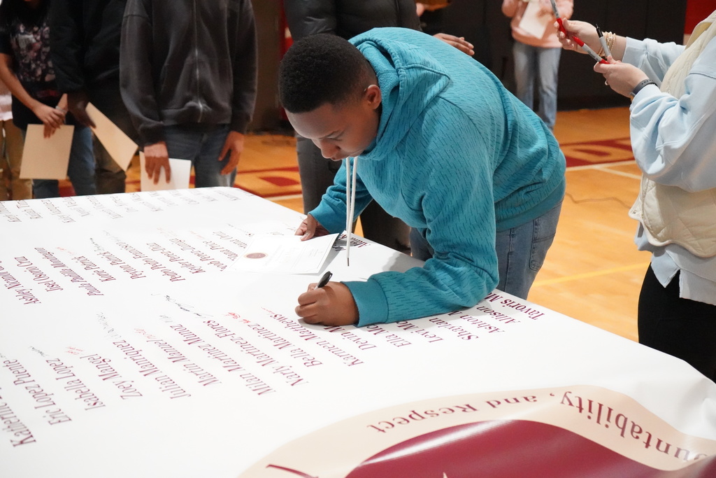 A student signs a banner during an award ceremony held inside a school gym.