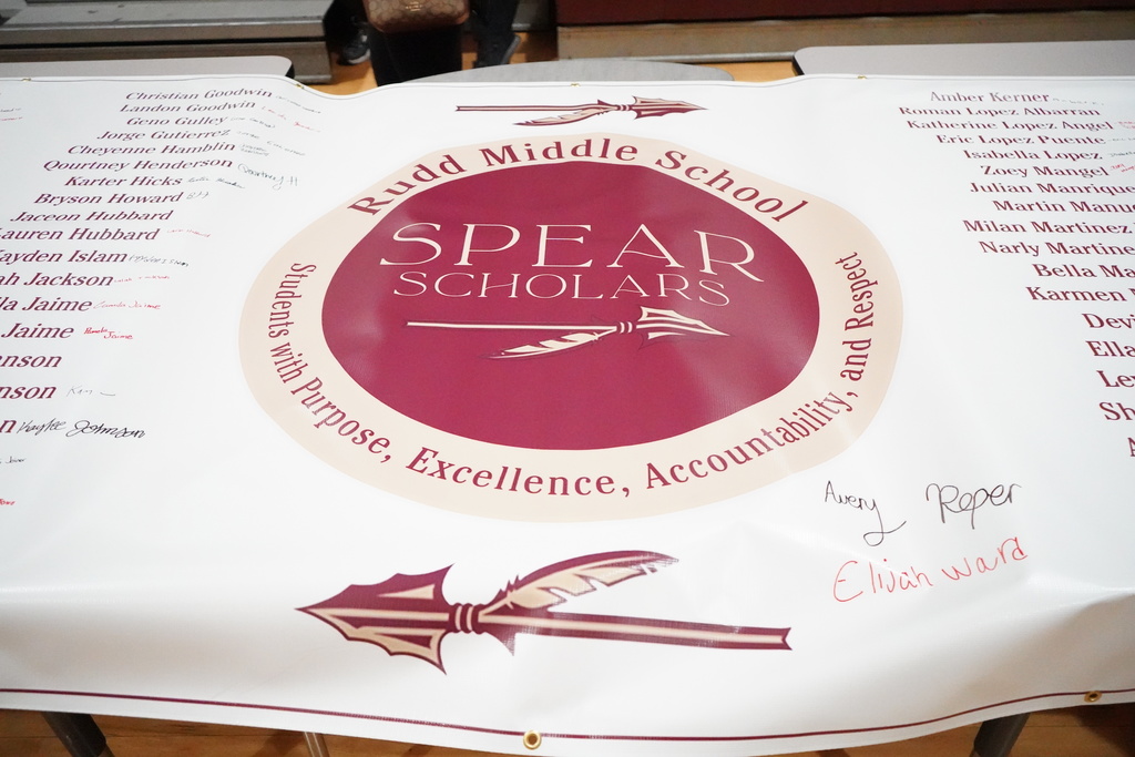 Image is of a large banner with Rudd Middle School students' names listed on it. Next to their names are their signatures. In the middle of the banner is the Rudd Middle School logo.