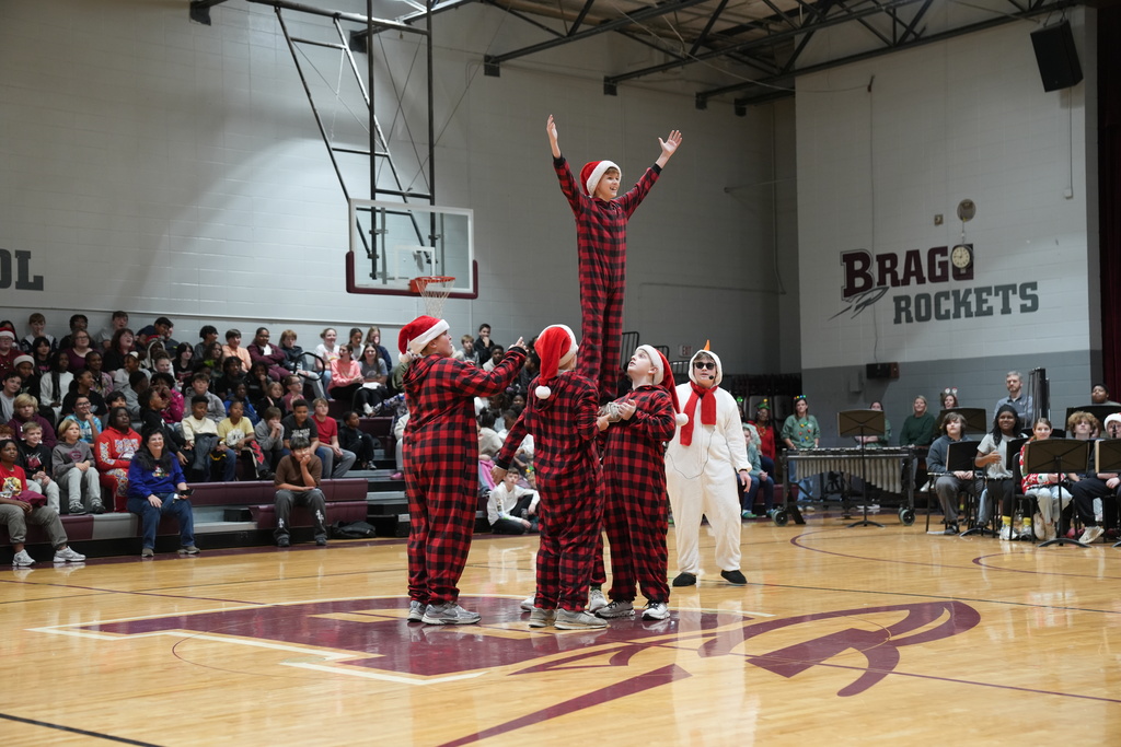 Image is from the Bragg Middle School Christmas Visions Pep Rally inside Bragg's gym. In the photo, students are lifting another student in the air while they all wear santa hats and christmas themed pajamas.
