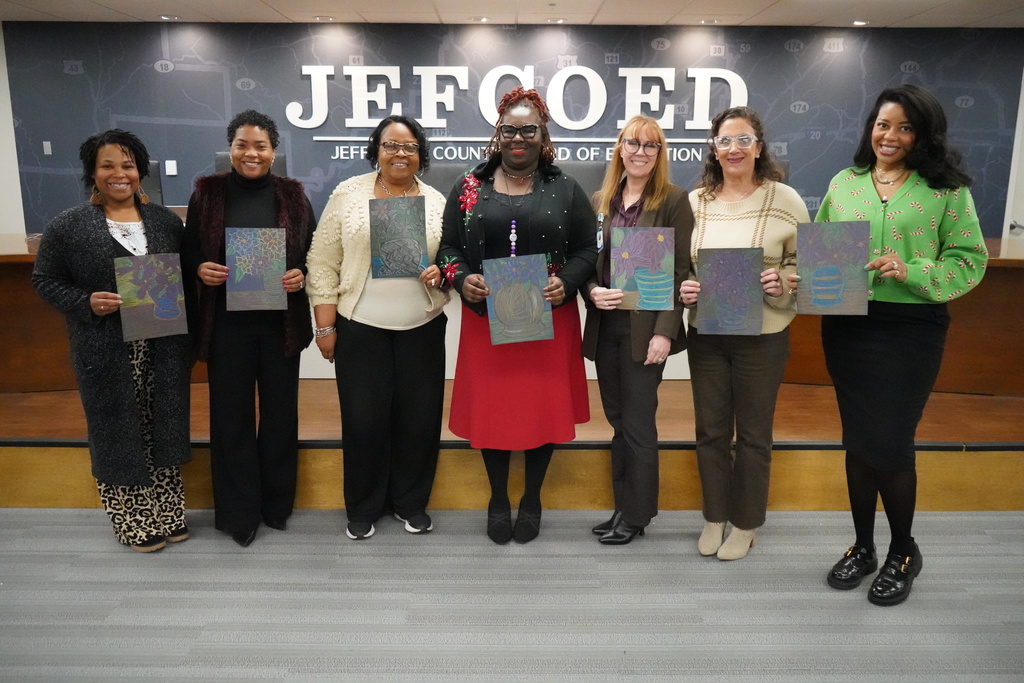 JEFCOED employees stand together in the JEFCOED board room and smile while holding construction paper with poinsettias drawn on them.