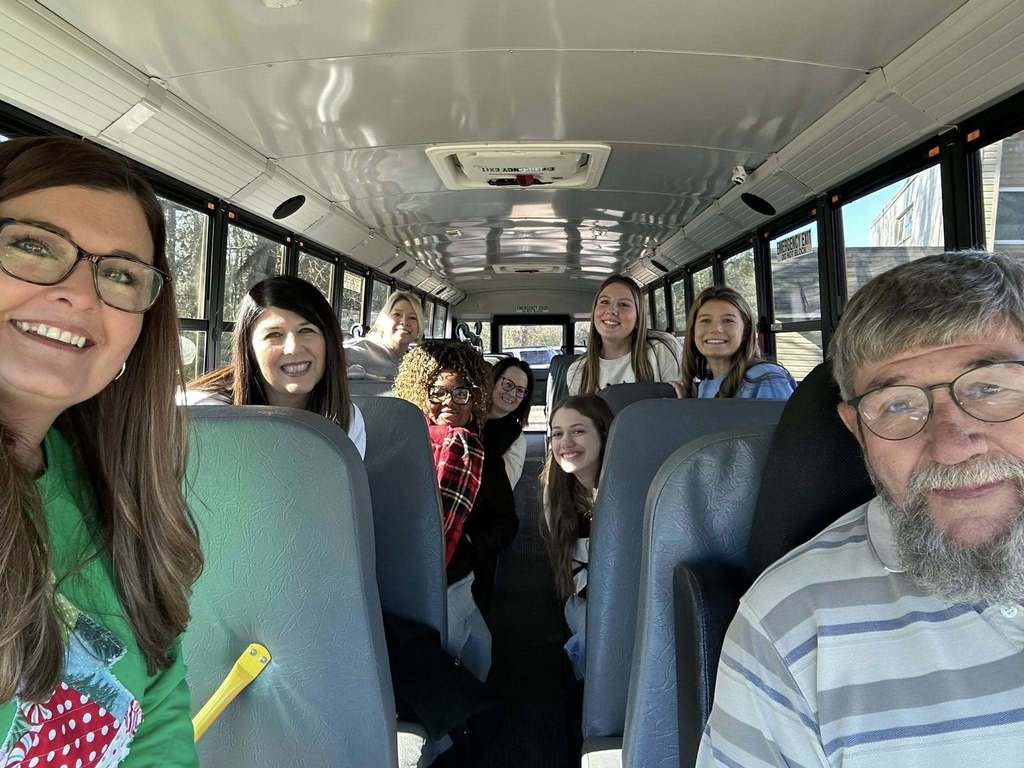 A group of women and a man smile in a selfie taken on a school bus.