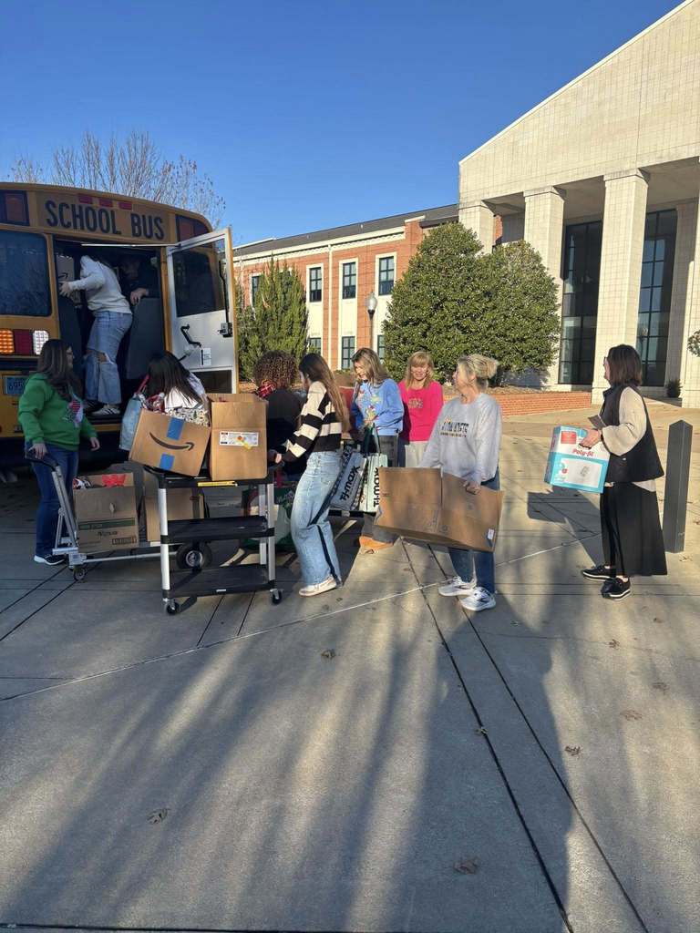 A group of women stand outside a school and load boxes into a school bus.