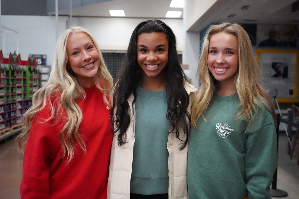 Three students stand together for a photo and smile while standing inside a Walmart.
