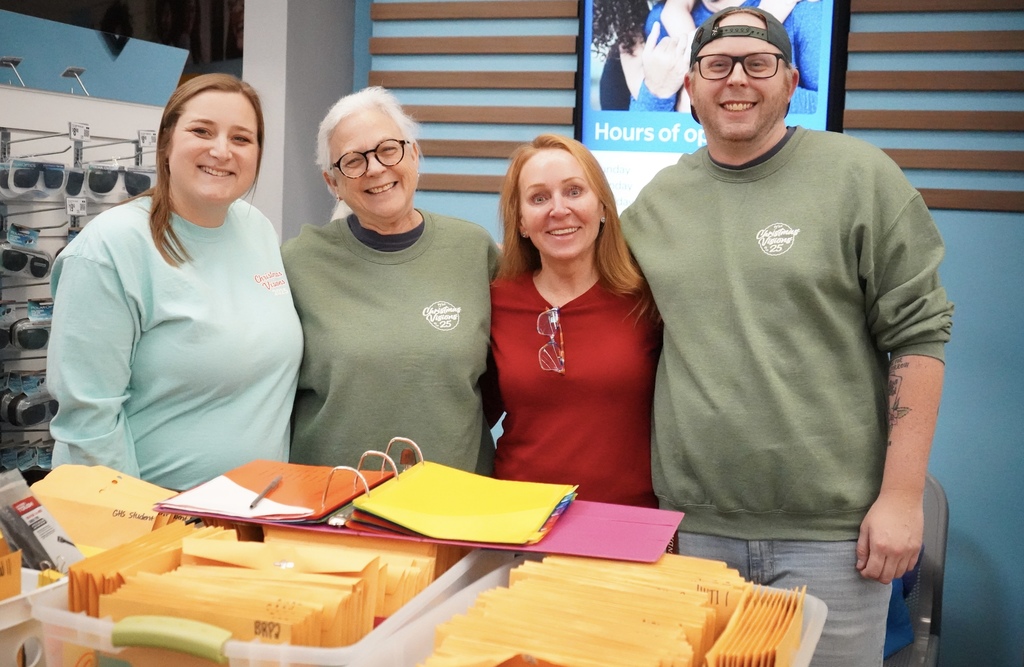 Adults stand together behind boxes filled with manillla folders and smile.