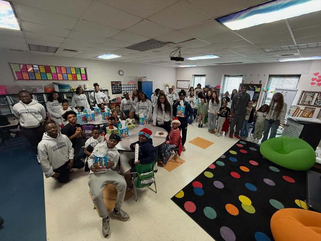 Clay-Chalkville High School and Clay Elementary School students stand and sit together for a photo inside a school classroom.