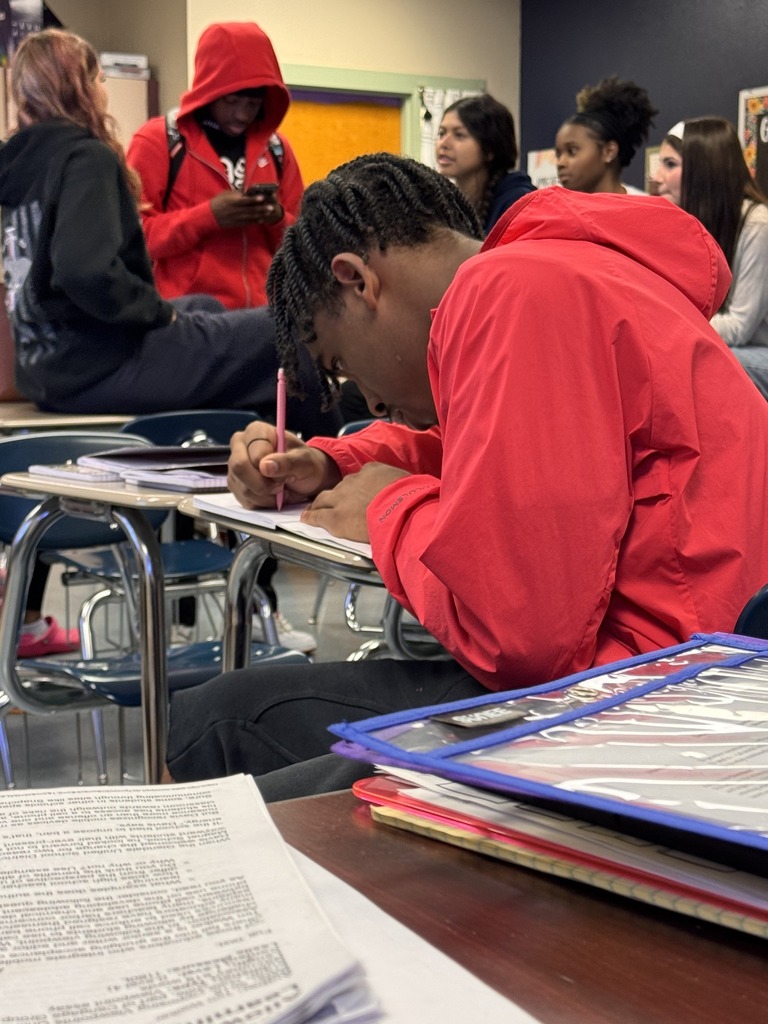 A student writes a letter inside a classroom.