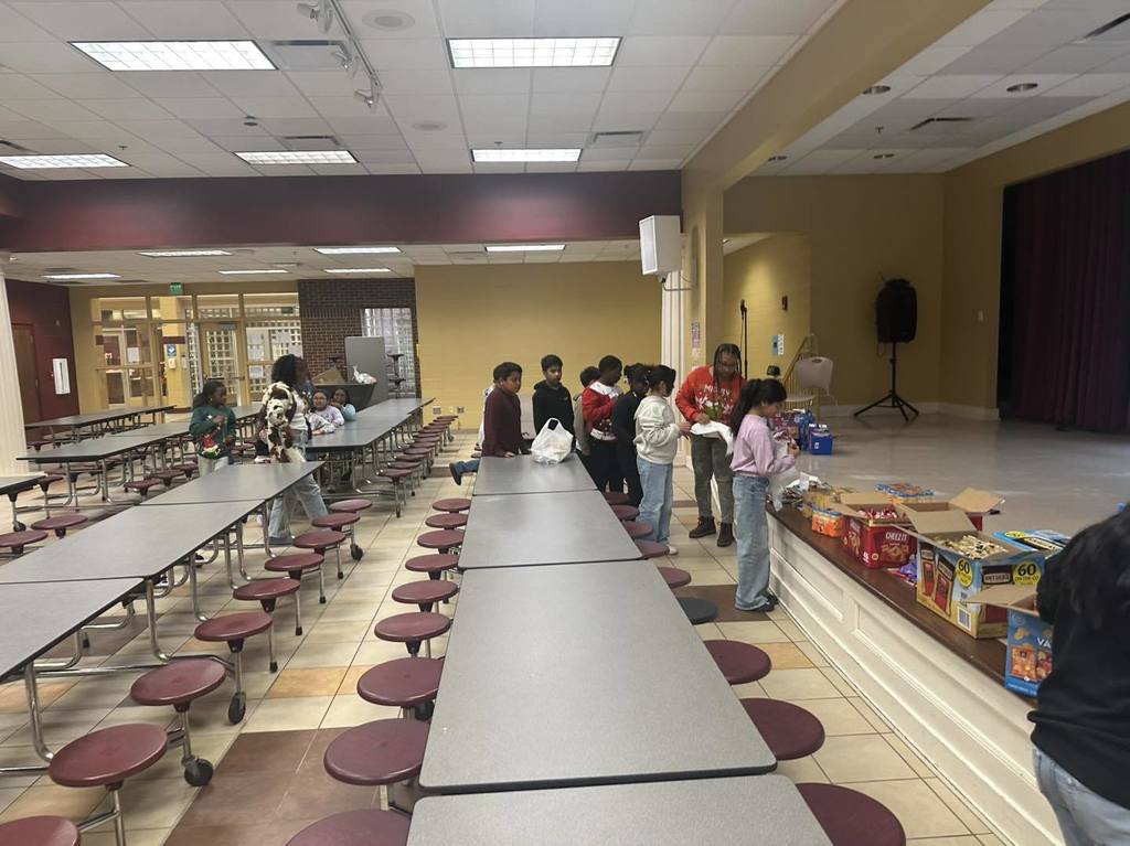 Brighton School Peer Helpers stand in a line in a lunchroom and put food items into bags.