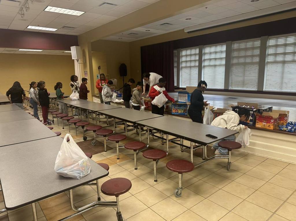 Brighton School Peer Helpers stand in a line in a lunchroom and put food items into bags.