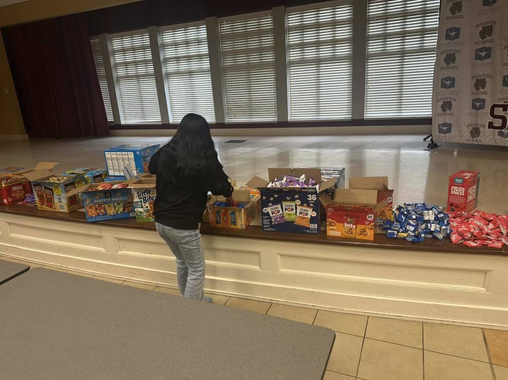 A Brighton School peer helper stands in a lunch room and places food items into bags.