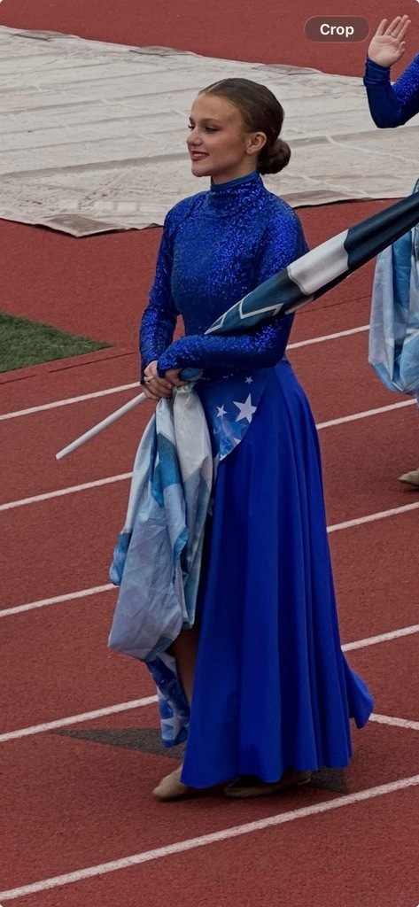 Gardendale High School student Kylie Thompson holds a flag and smiles while standing on a track. She wears a long blue dress with sparkles on the top.