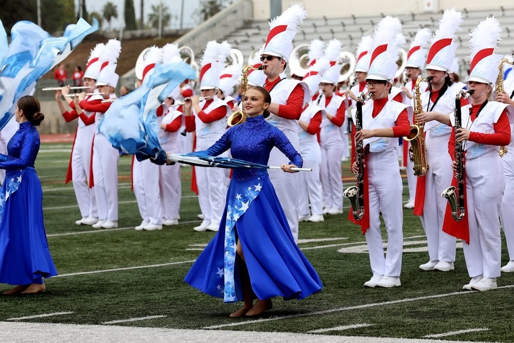 Gardendale High School student Kylie Thompson smiles while holding a flag and performing with a band on a football field.