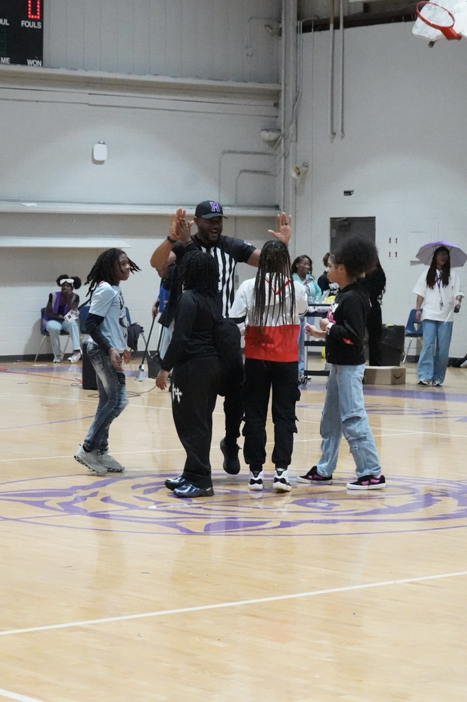 A man wearing a hat with the letter "M" on it high-fives Minor Middle School students in the school gym.