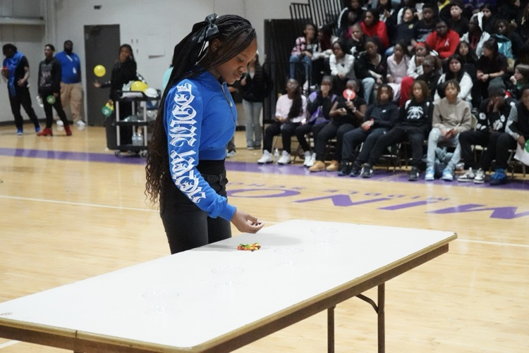 A student stands at a table in a school gym and holds skittles.