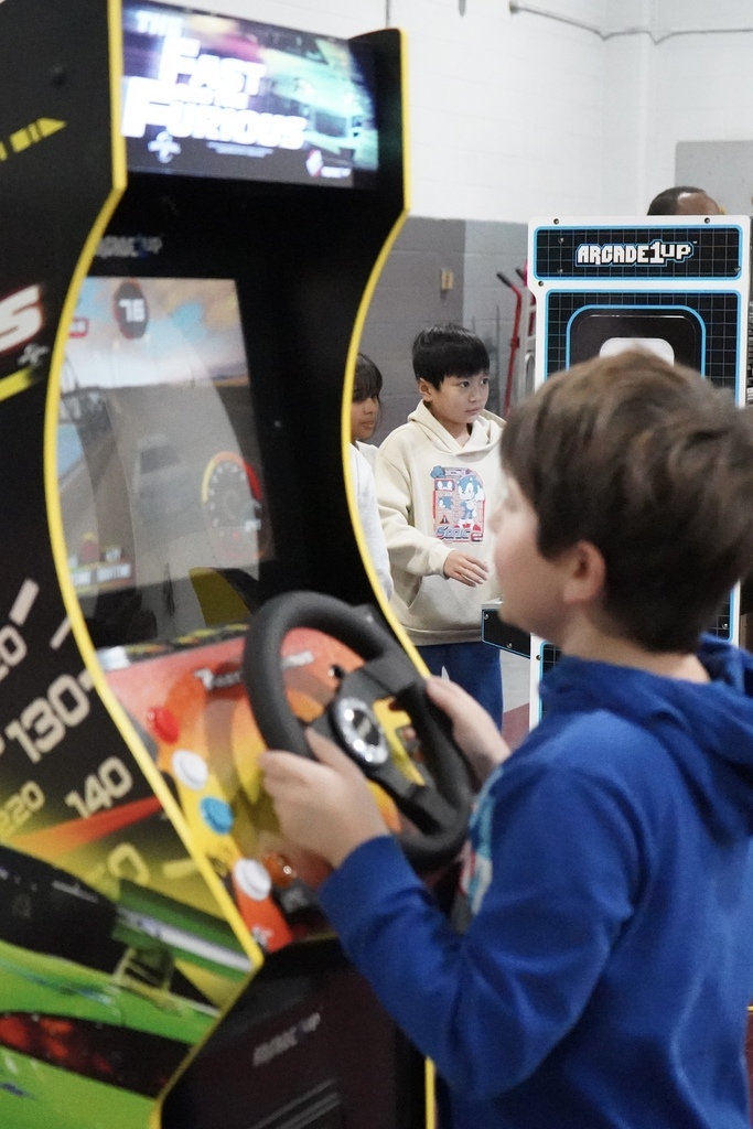 Students play arcade-style video games inside a school gym.