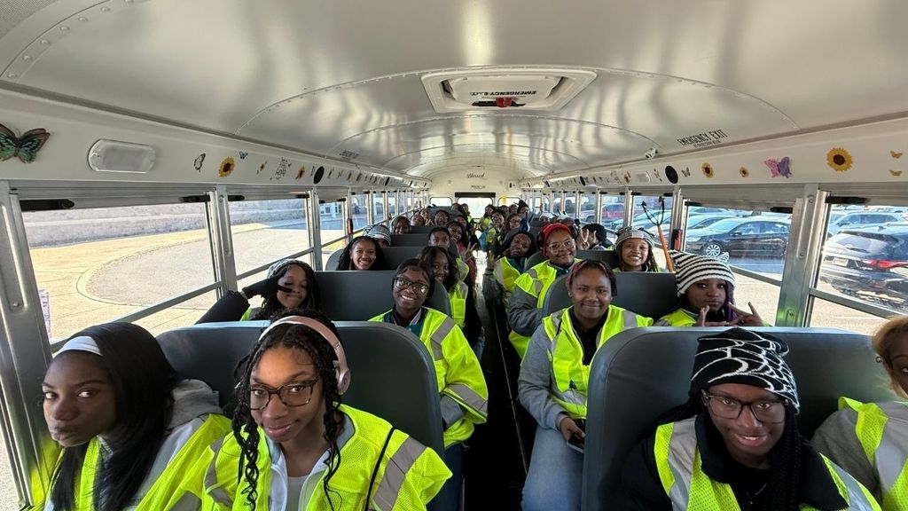 Young people sit in a school bus and wear yellow work vests.