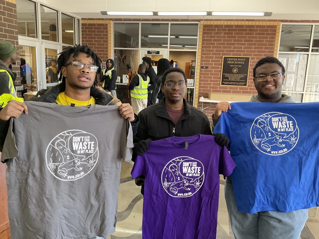 Three young men hold up anti-litter shirts while they stand in the lobby of Center Point High School, preparing for a community cleanup event.