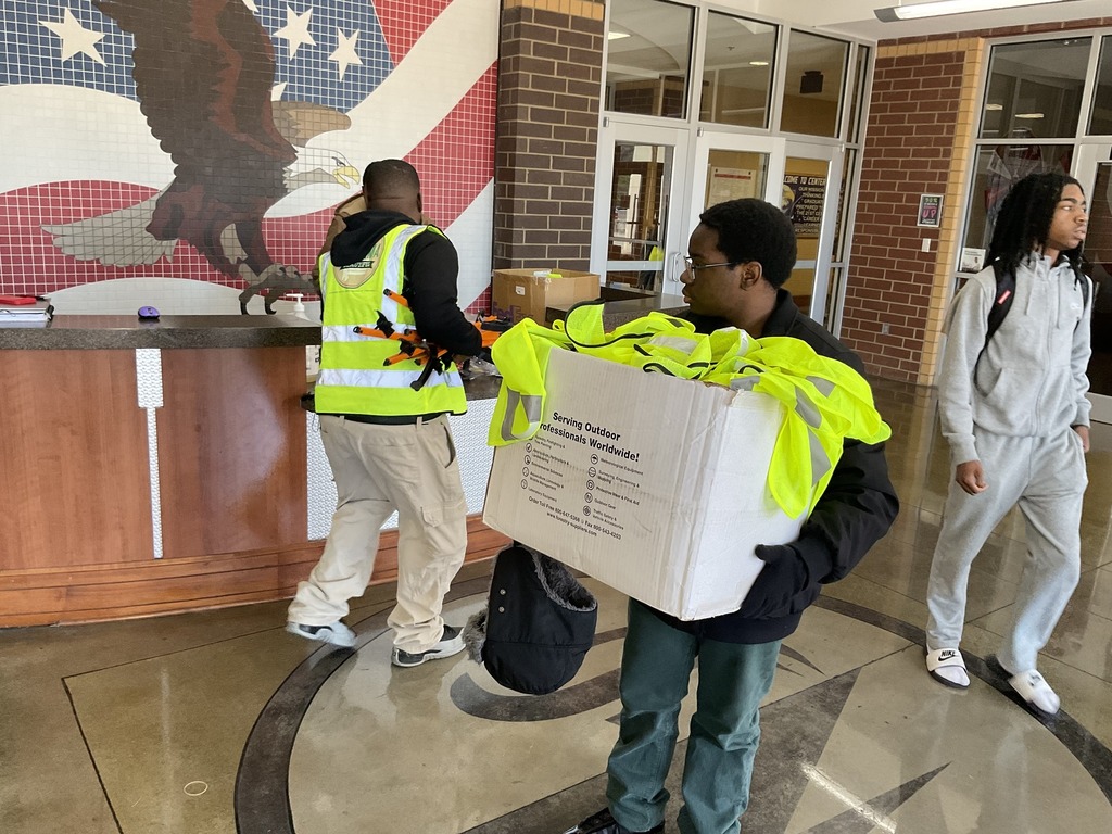 A young man holds a box of yellow work vests while standing in the lobby of Center Point High School.