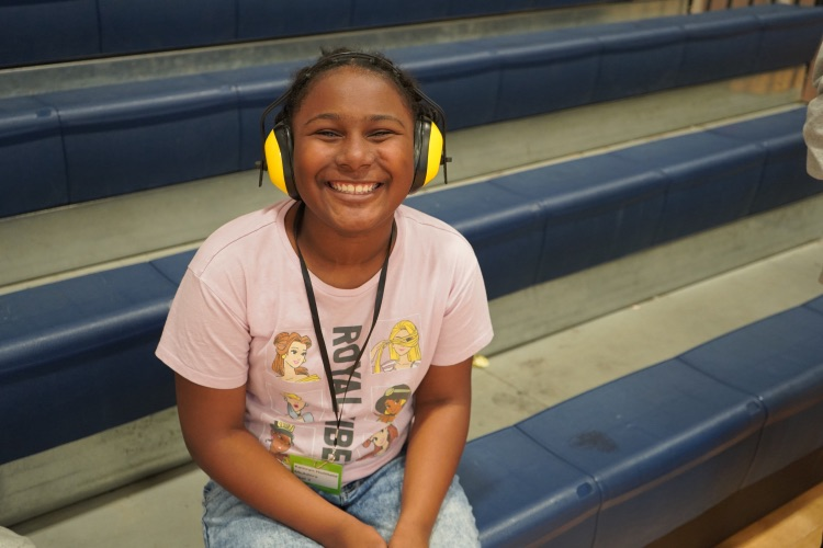 A girl smiles while sitting on bleachers in a school gym. 