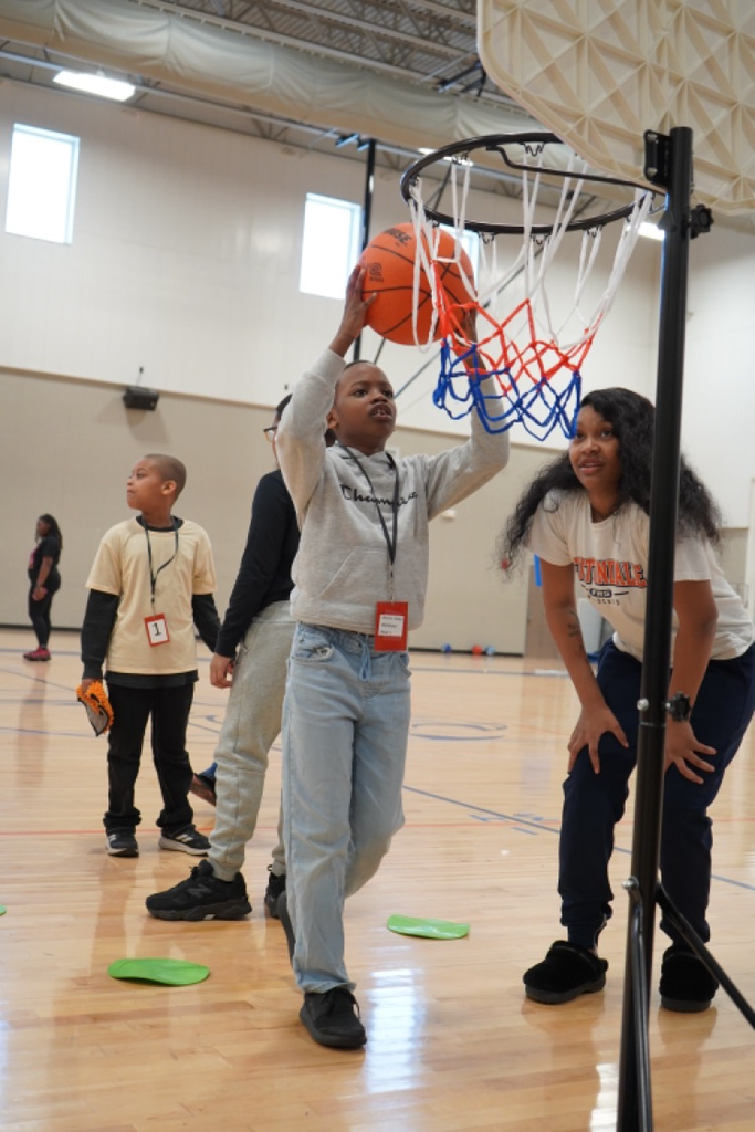 A student throws a basketball into a hoop while other students and a Fultondale High School basketball player stand around him.