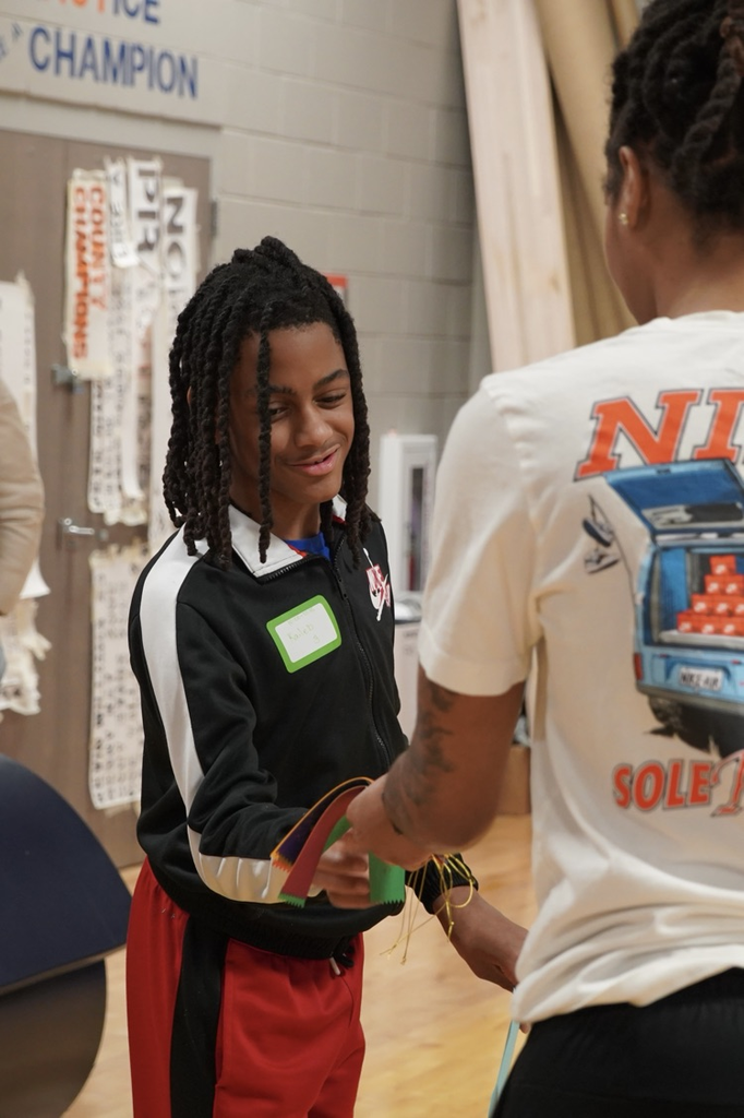 A boy smiles while being handed a ribbon. 
