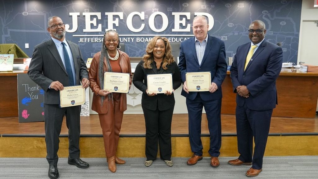 Jefferson County School board members stand together for a photo in the board room while holding certificates.