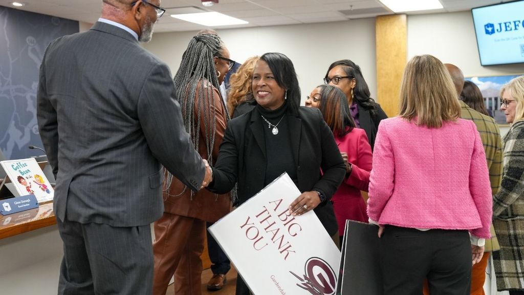 Gardendale Elementary School's principal shakes hands with Mr. Walter Curry while holding a large thank you note inside the JEFCOED board room.