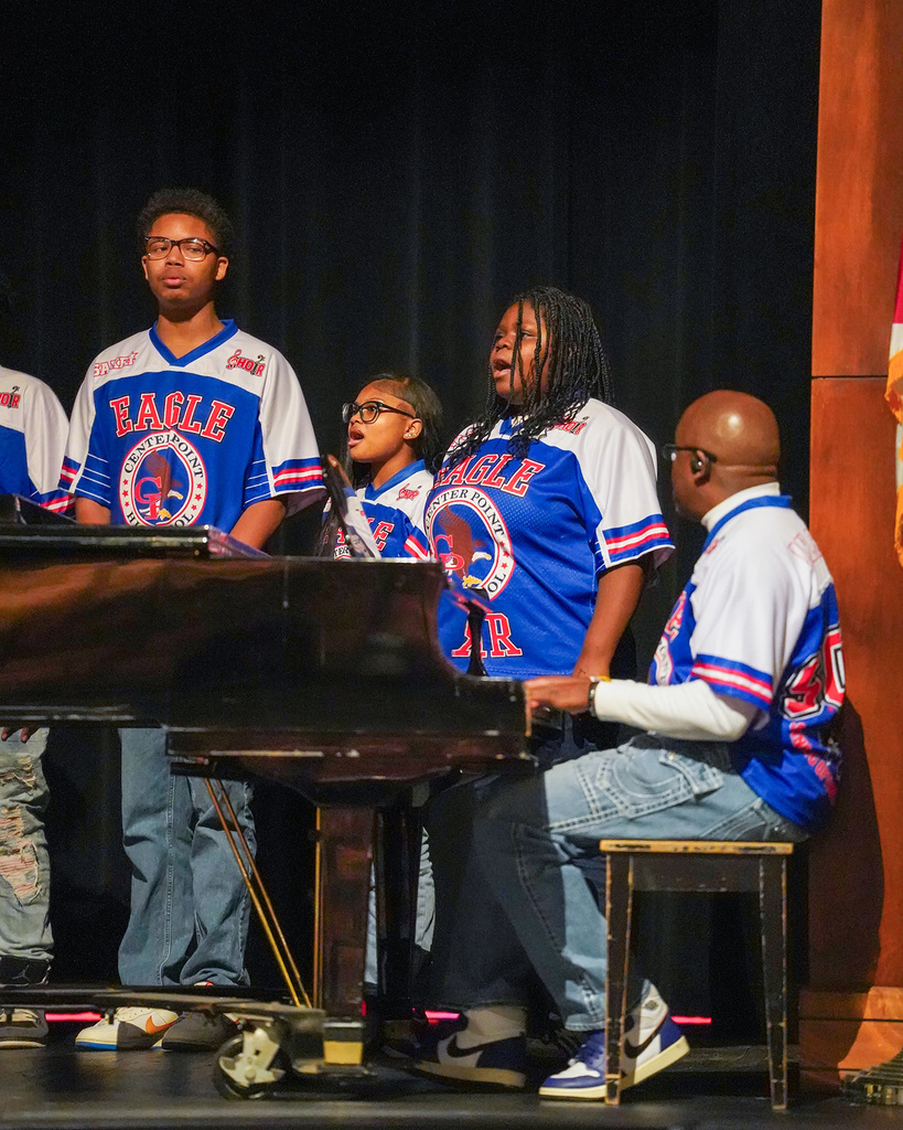 Members of the Center Point High School choir perform on stage. Their director is playing a grand piano. 