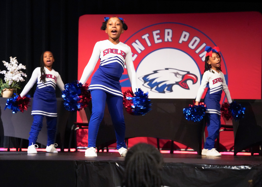 .Three young girls perform on stage as part of the Eaglettes dance team. They are wearing red, white, and blue "Eagles" uniforms. 