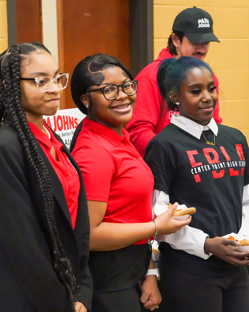 Three high school students wearing red and black for FBLA participate in a community event. The student in the middle is smiling at the camera. 