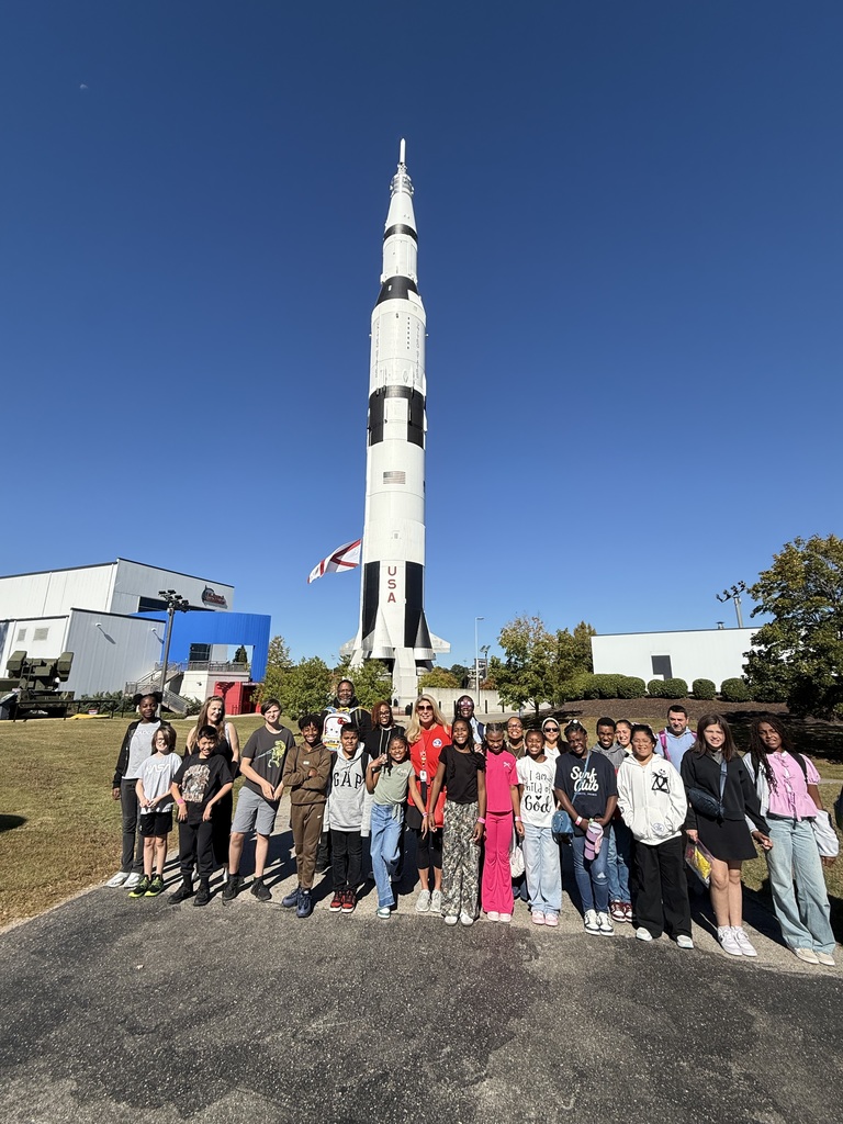 A group of school students stand in front of a rocket. 