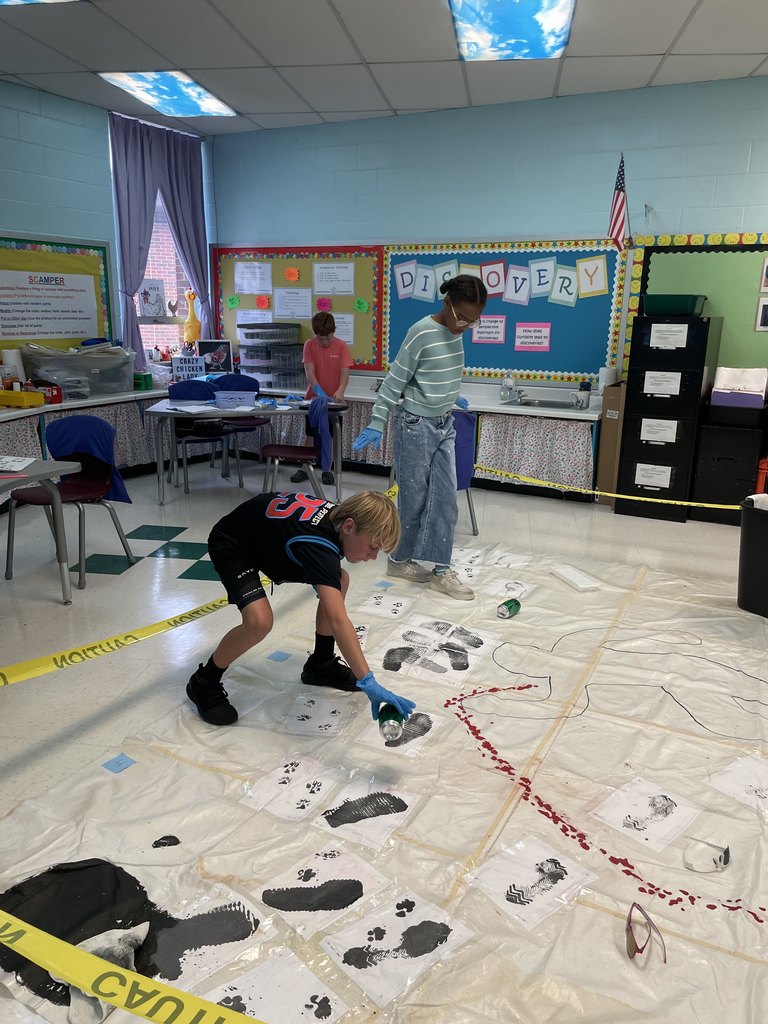 A group of young students is investigating a pretend crime scene. They are tracing footprints on the floor. 
