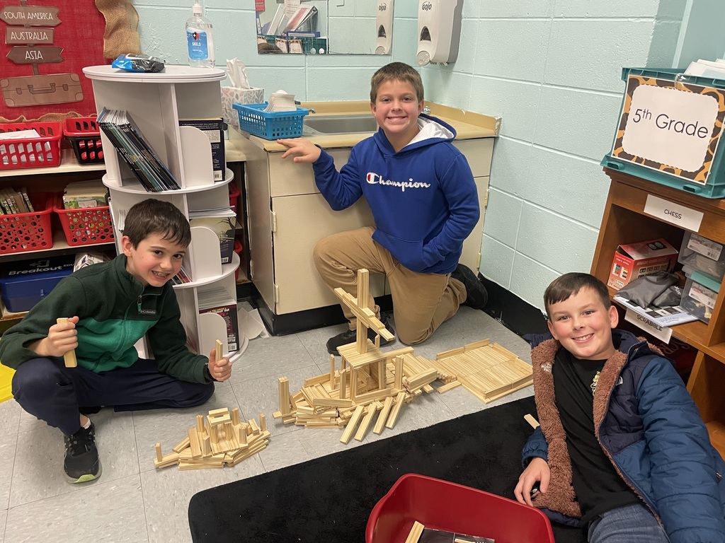 Three boys build with wood planks on the floor. It looks like they have build a ship. 