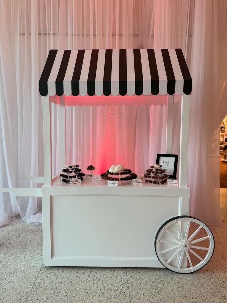 A cart with a black and white striped cover on it holds hand-made sweets.