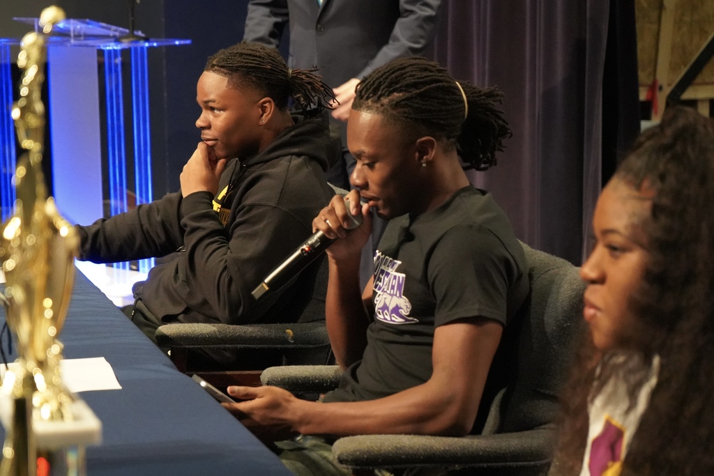 Clay-Chalkville High School student Brayden Butler speaks into a microphone while sitting at a table with two other students on National Signing Day.