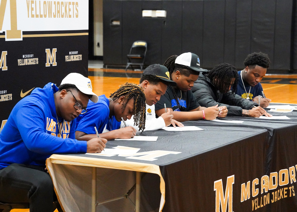 Six young men lean over as they sign a paper on National Signing Day at McAdory High School. 