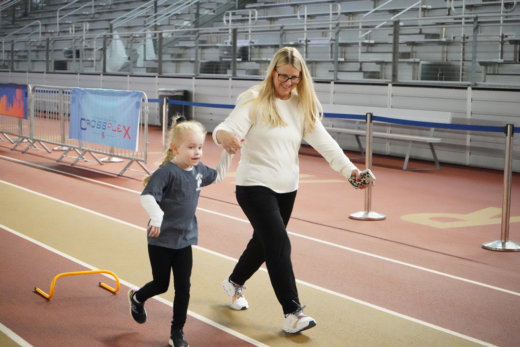 An adult runs with a child while holding her hand as the child participates in the Elementary ExEd Track and Field day at the Birmingham Crossplex.