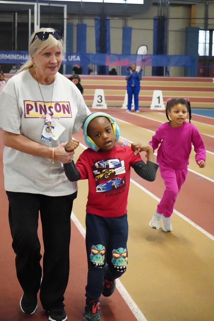 A teacher helps a student run down a track as another child runs by during the Elementary ExEd Track and Field day at the Birmingham Crossplex.