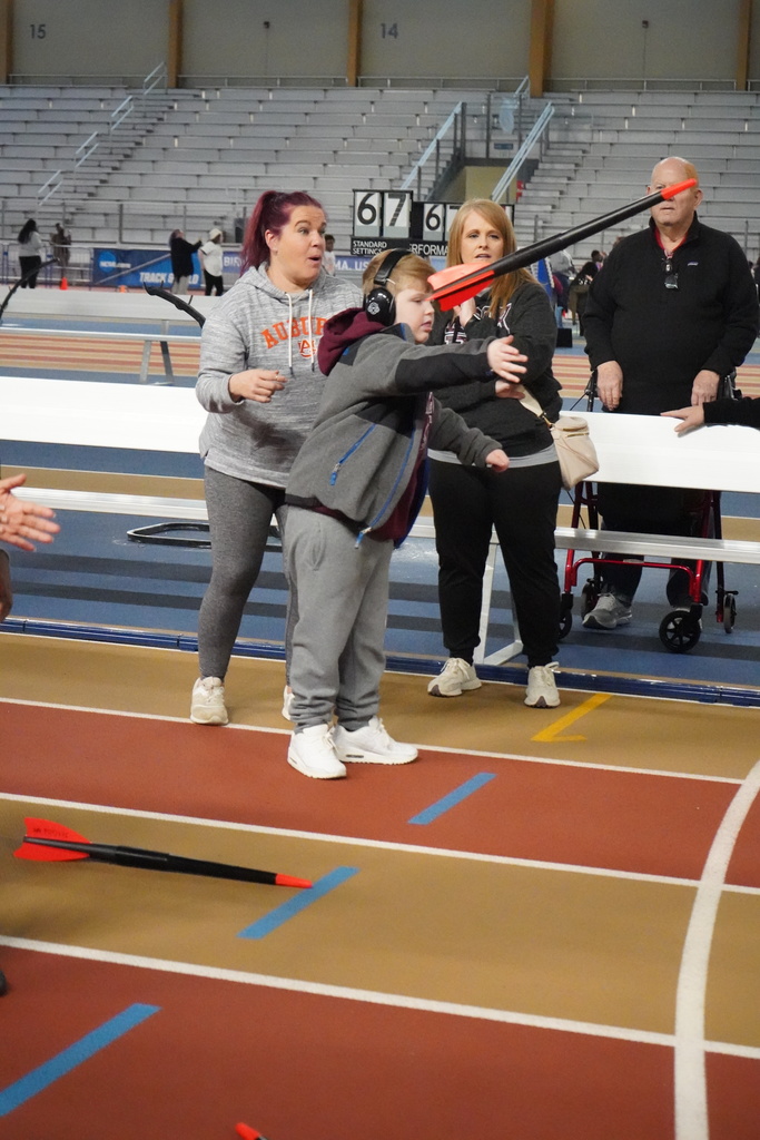 A student throws a javelin at the Elementary ExEd Track and Field day at the Birmingham Crossplex. Three adults stand behind him as he throws.