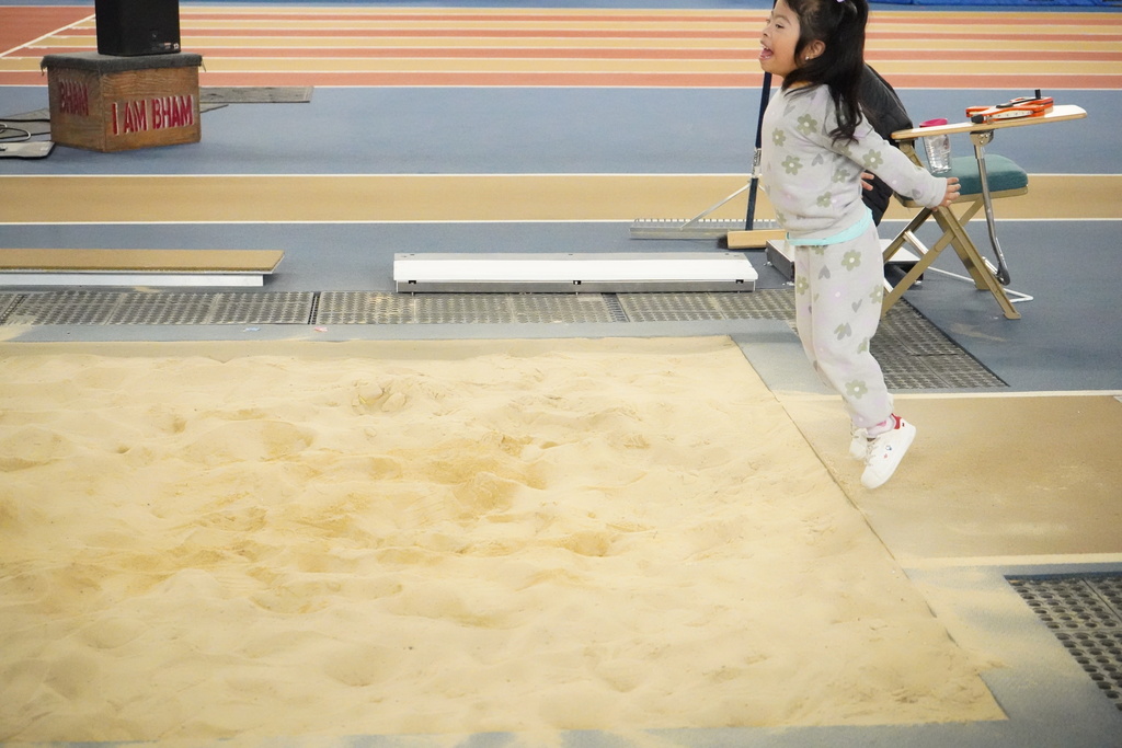 A girl does a long jump into a sand pit at the Elementary ExEd Track and Field day at the Birmingham Crossplex.